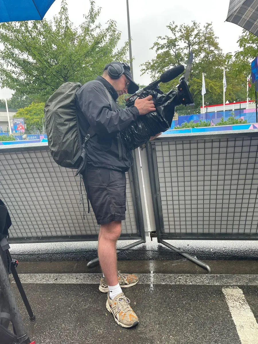 On set of Breaking Barriers: a camera operator filming over a railing at a sports venue