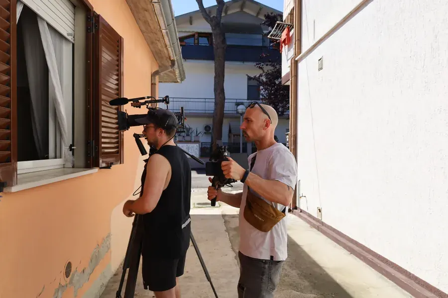 On set of Breaking Barriers: two crew members with camera and boom microphone beside a house wall