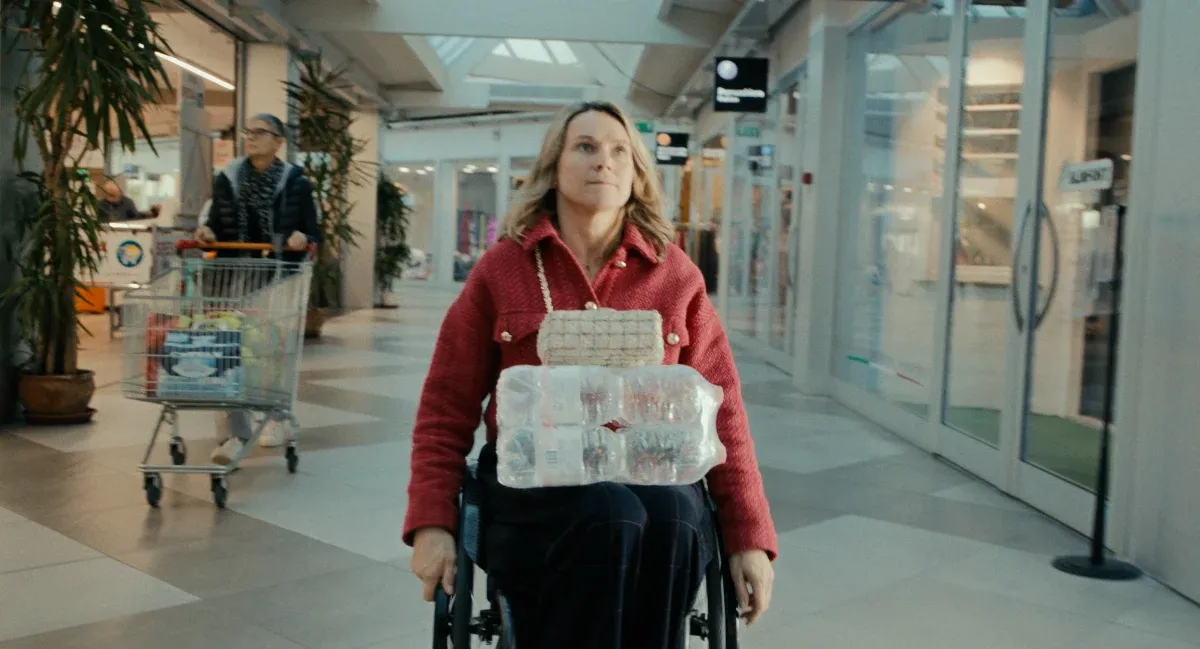 Film still from Breaking Barriers: Svetlana Moshkovich crossing a shopping arcade in her wheelchair, a pack of water bottles on her lap